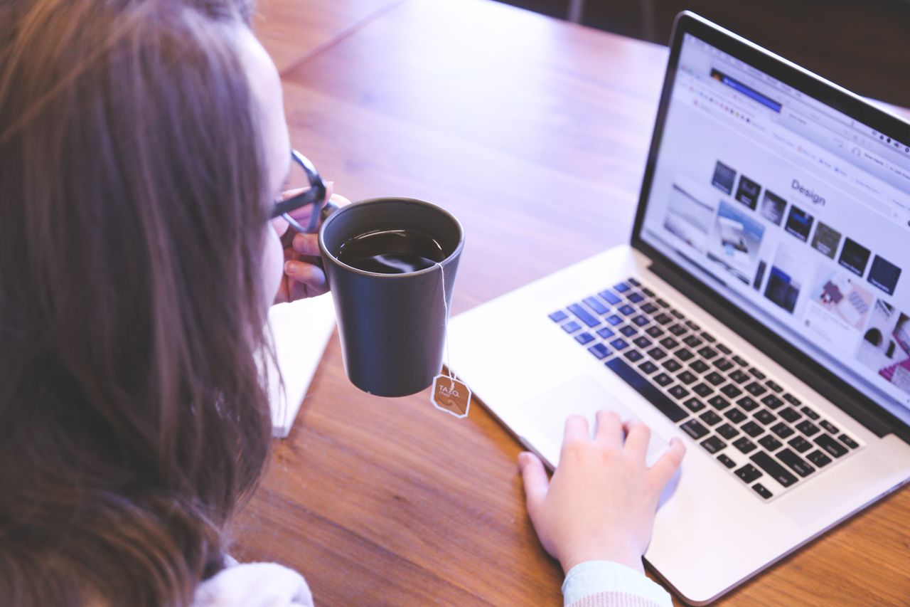 Une femme savoure un café tout en naviguant sur le web sur un ordinateur portable installé à un bureau de travail à domicile.